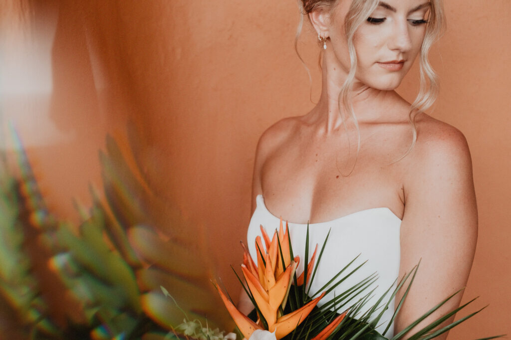 Bride holding bird of paradise bouquet at Casa Cosmos Puerto Vallarta wedding, white strapless gown, terracotta wall