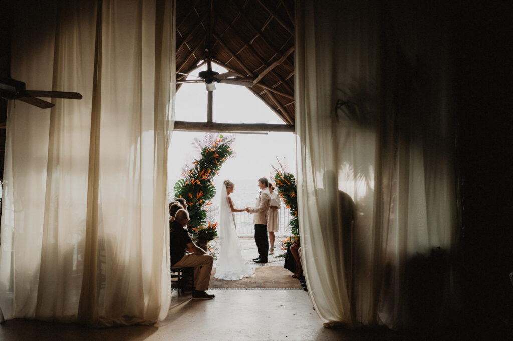 Wedding ceremony at Casa Cosmos Puerto Vallarta, couple exchanging vows under tropical floral arch with ocean view