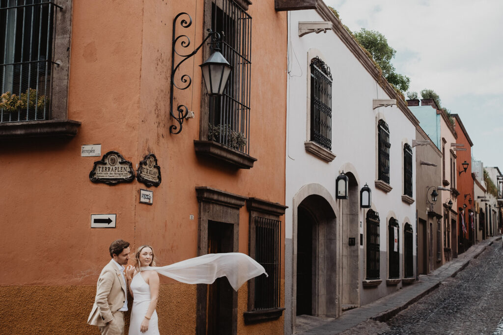 Bride and groom walking cobblestone street in San Miguel de Allende, veil caught by wind, wedding day