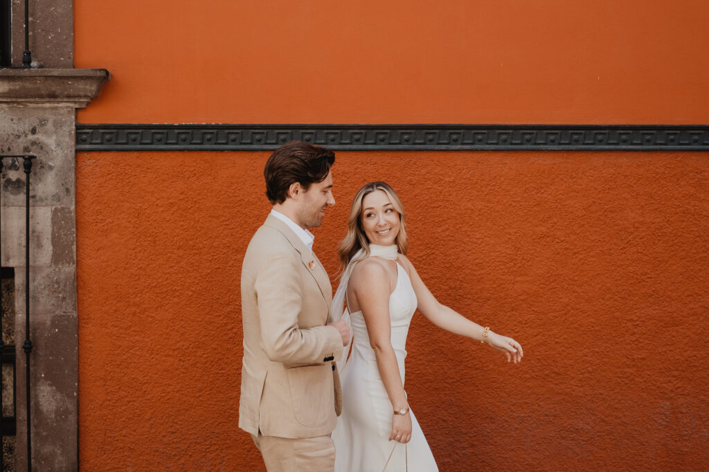 Bride and groom walking hand in hand against a terracotta wall in San Miguel de Allende wedding