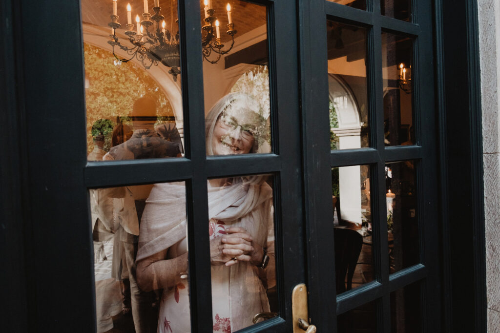 Elderly guest smiling through glass door at San Miguel de Allende wedding reception, candlelit interior