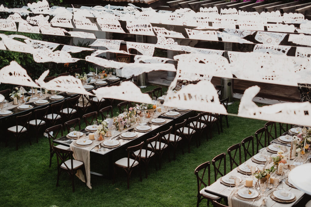 Outdoor wedding reception tables with papel picado overhead on green lawn, San Miguel de Allende
