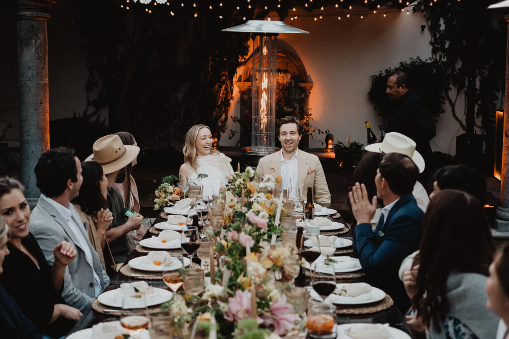 Wedding reception dinner at a candlelit courtyard in San Miguel de Allende, couple laughing at long floral table
