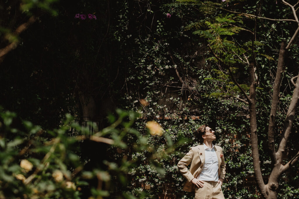 Groom in linen suit stands among lush gardens, San Miguel de Allende wedding, documentary film photography