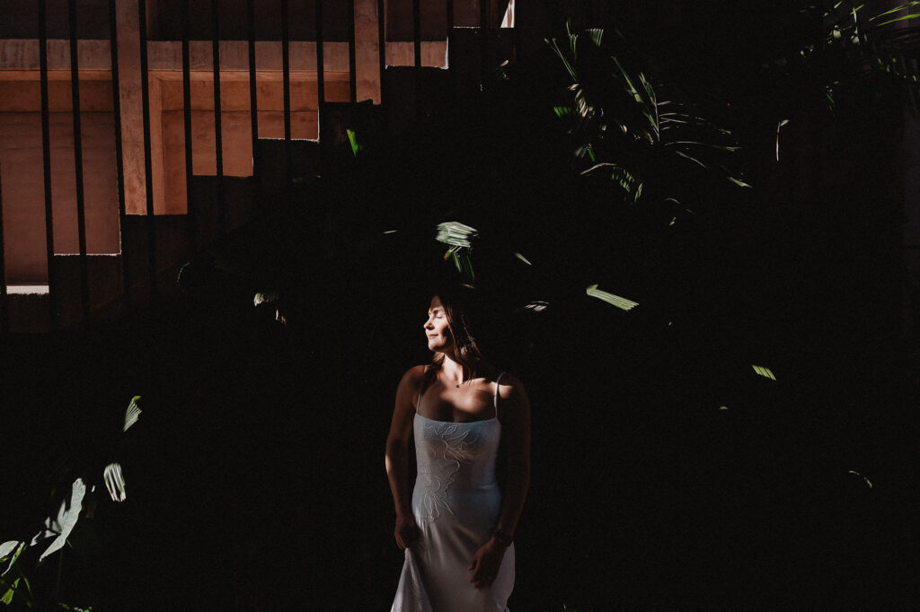 Bride in white gown bathed in dappled sunlight among tropical plants, elopement at Rosa Morada San Pancho Mexico