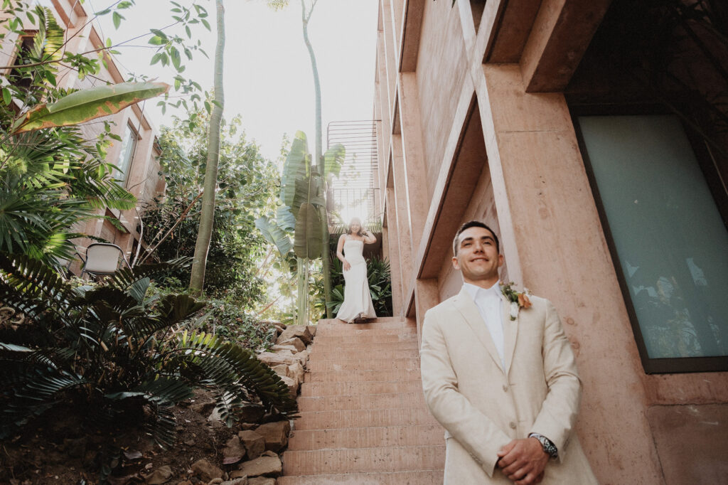 Groom in cream suit waits as bride descends stone stairs at Rosa Morada, San Pancho elopement