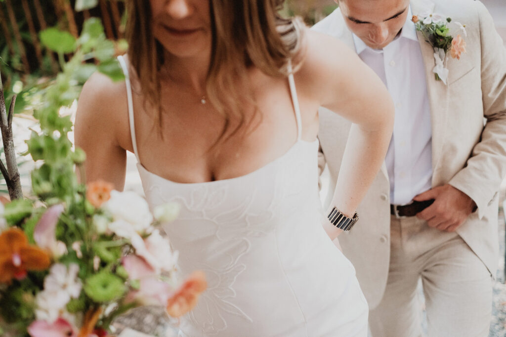 Bride in white slip dress holding bouquet walks with groom in beige suit at San Pancho elopement