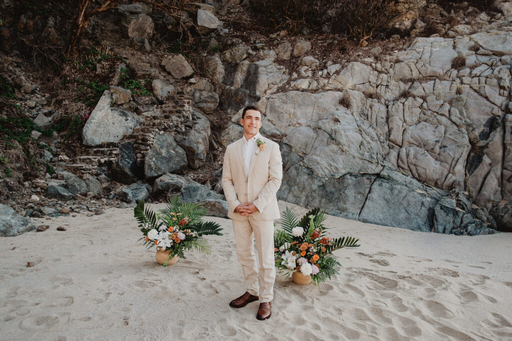Groom in linen suit standing on beach at Rosa Morada, San Pancho elopement with tropical floral arrangements