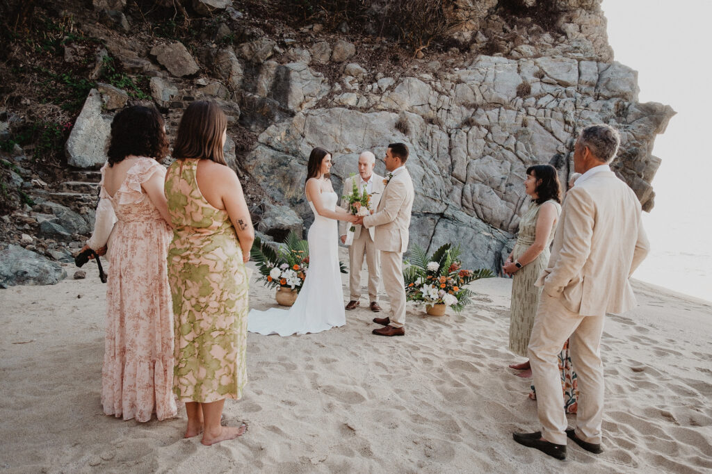 Intimate beach elopement ceremony at Rosa Morada, San Pancho, with couple exchanging vows before rocky cliffs