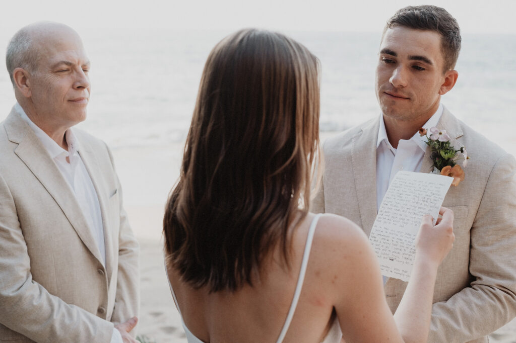 Groom listening to bride read vows at beach elopement, Rosa Morada San Pancho Mexico