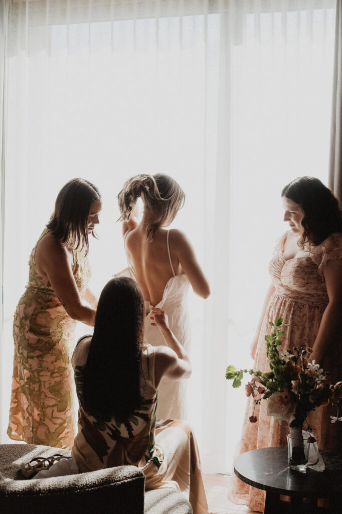 Bride getting dressed by bridesmaids in soft window light, elopement at Rosa Morada, San Pancho Mexico