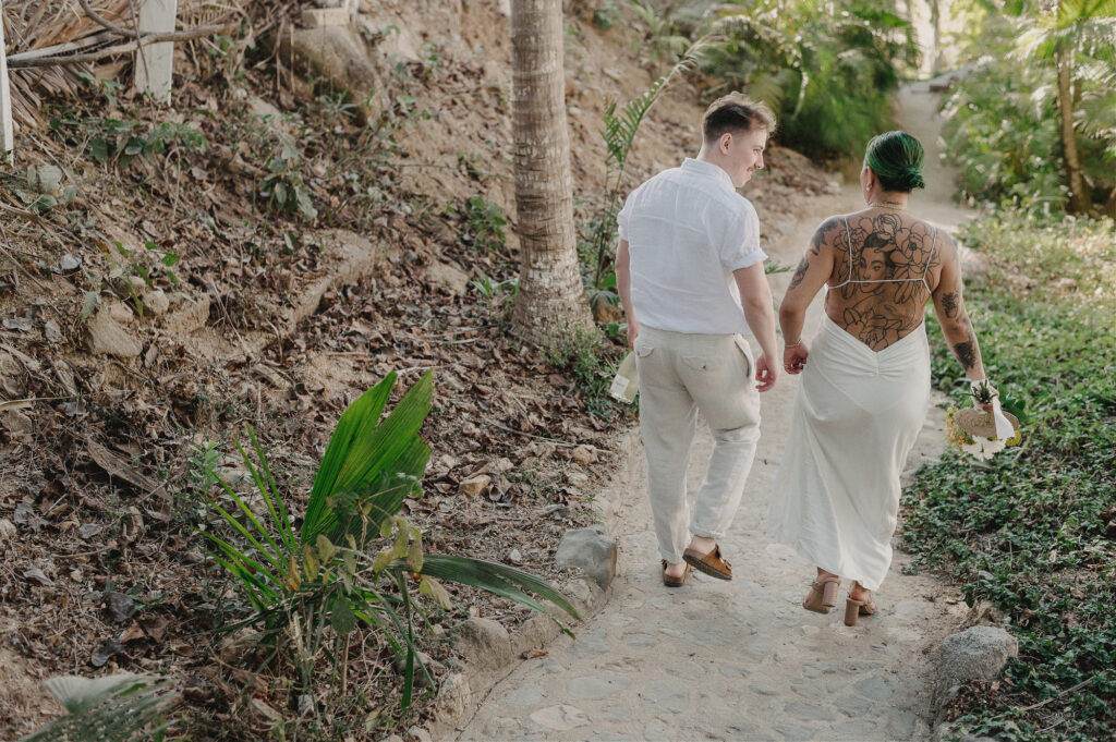 Couple walking hand in hand down a jungle path at Villa Amor Sayulita elopement, bride in backless dress with tattoos