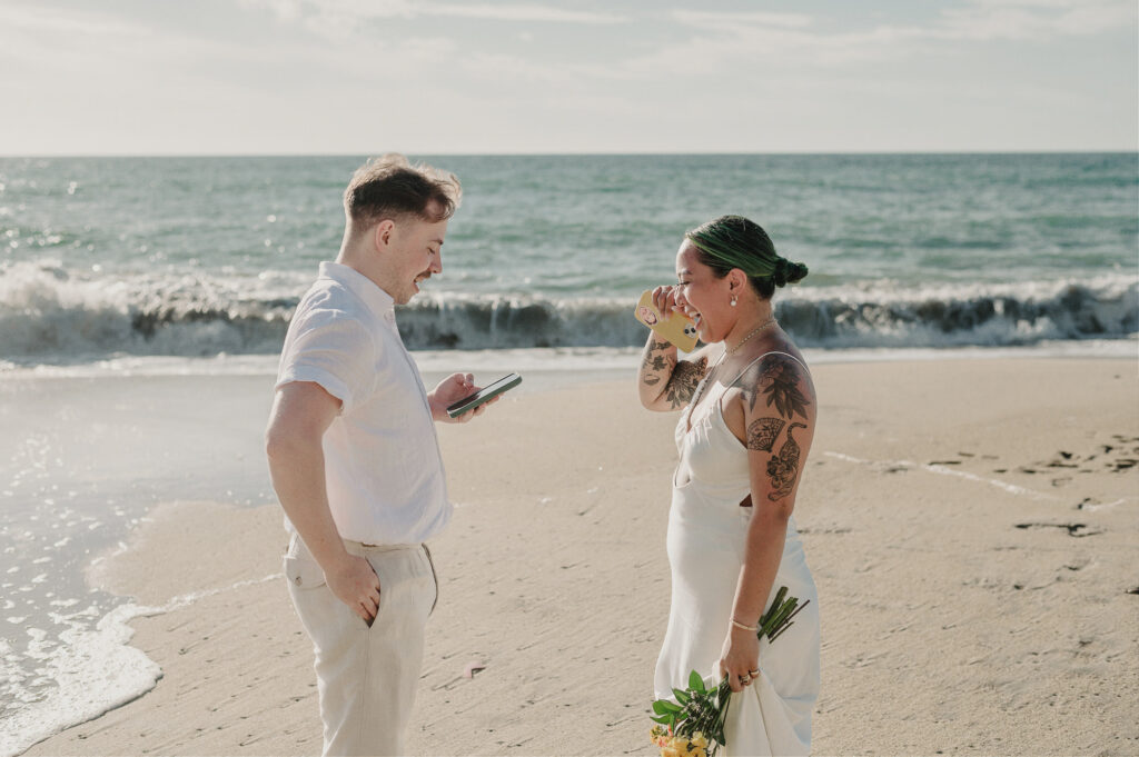 Groom reads vows from phone while bride cries happy tears during beach elopement in Sayulita Mexico