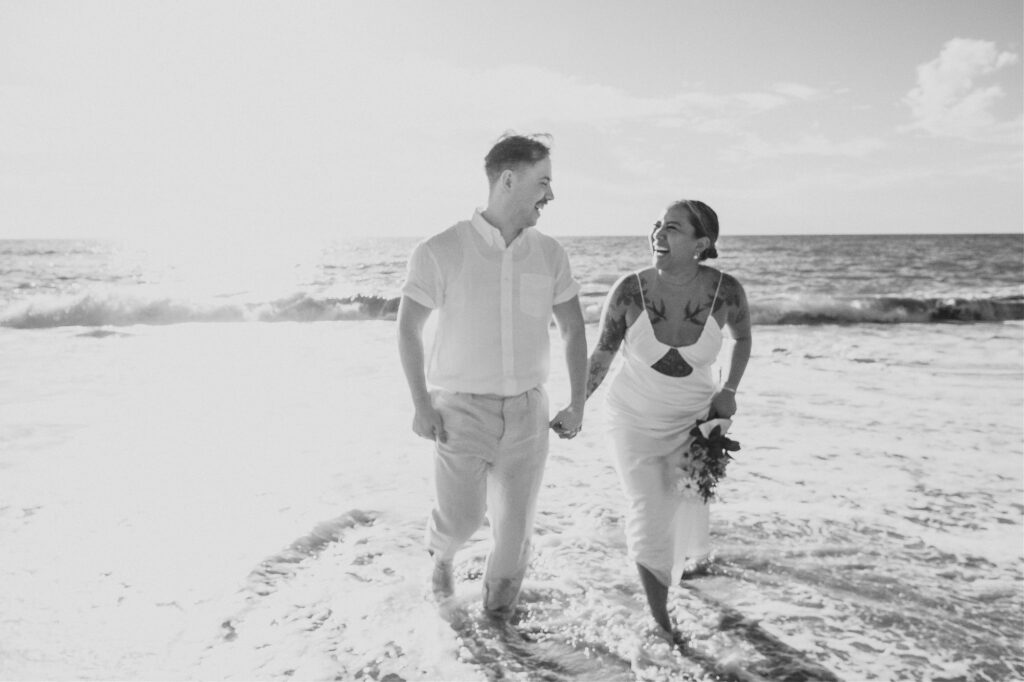 Couple laughing and walking through ocean waves during beach elopement at Villa Amor Sayulita Mexico