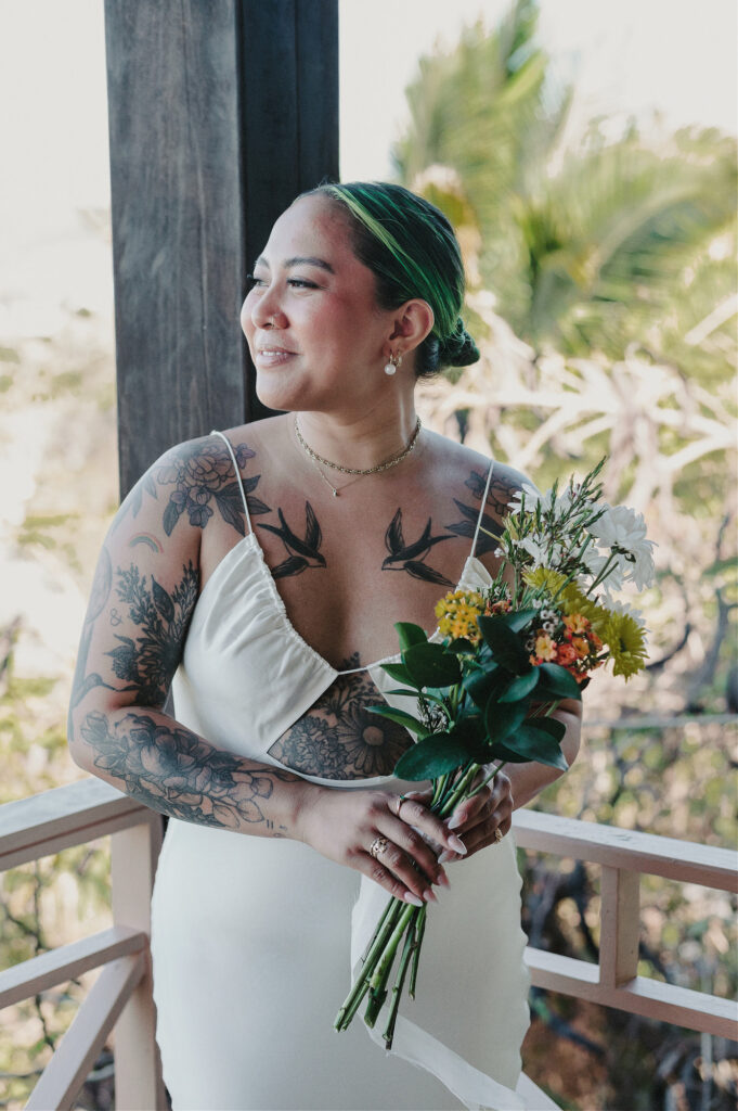 Tattooed bride in white gown holding wildflower bouquet on balcony at Villa Amor Sayulita elopement