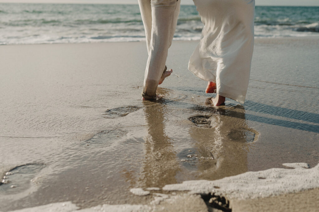Barefoot couple walking on wet sand at Sayulita beach during elopement, white linen pants, ocean waves