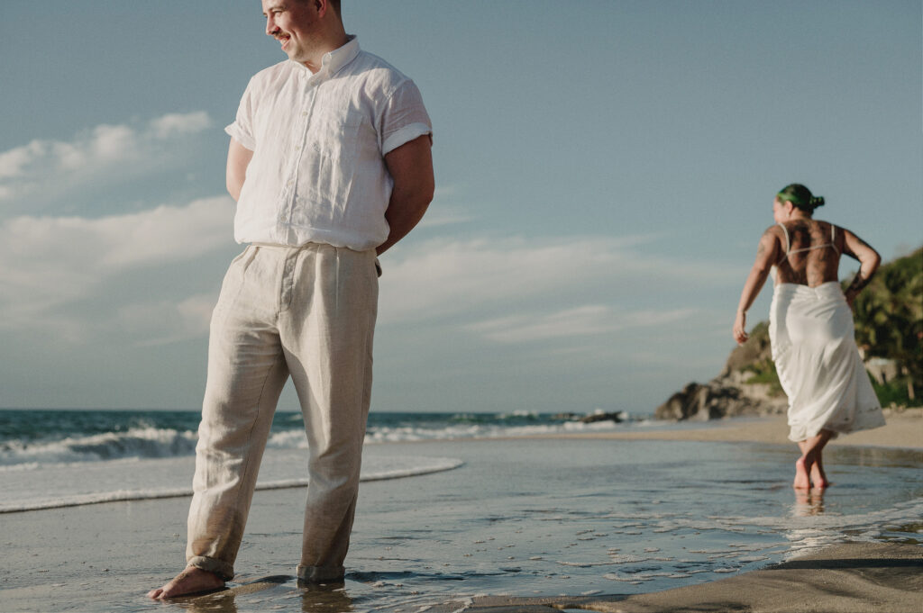 Groom smiling on shore at Villa Amor Sayulita elopement, partner walking in background