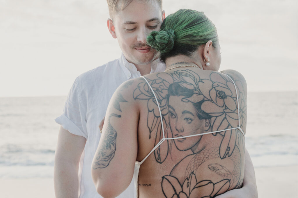 Couple embracing on beach at Villa Amor Sayulita elopement, woman with green hair and back tattoos