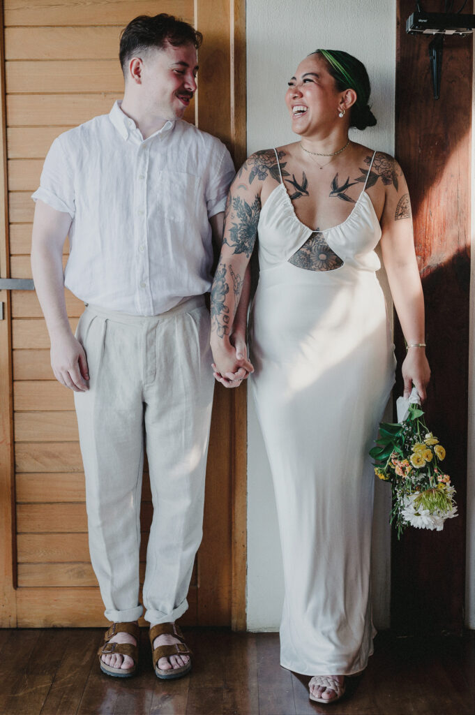 Couple laughing and holding hands in white outfits at Villa Amor Sayulita elopement, bride holding wildflower bouquet