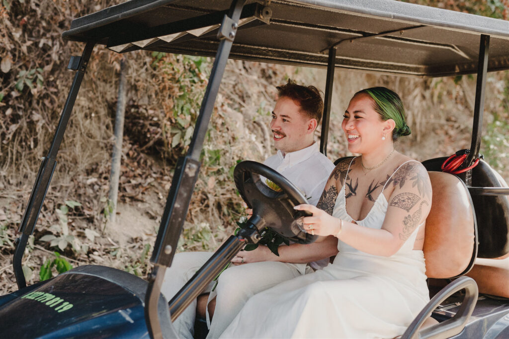 Bride and groom laughing in a golf cart at Villa Amor Sayulita elopement, bride in white dress with tattoos and green hair