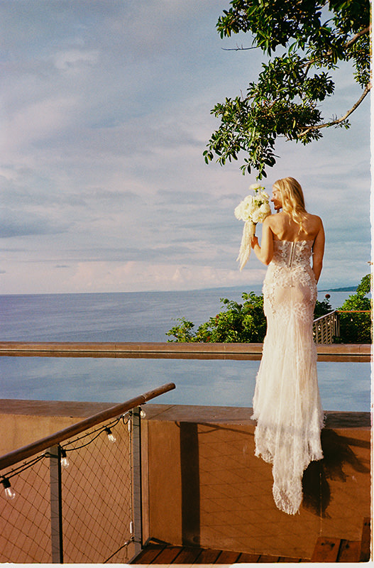 Bride in lace gown holding white bouquet overlooking ocean at One&Only Mandarina, Mexico wedding