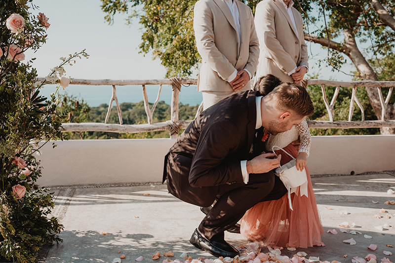 Groom kneeling to embrace flower girl at outdoor wedding ceremony, Villa Valentin Sayulita Mexico