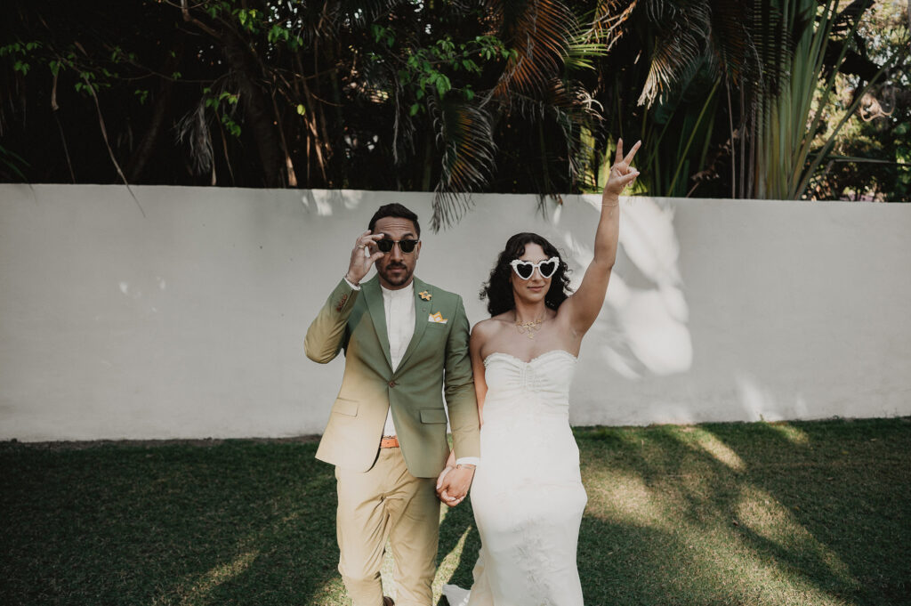Bride and groom in sunglasses laughing and holding hands at Frente al Punto wedding in Sayulita