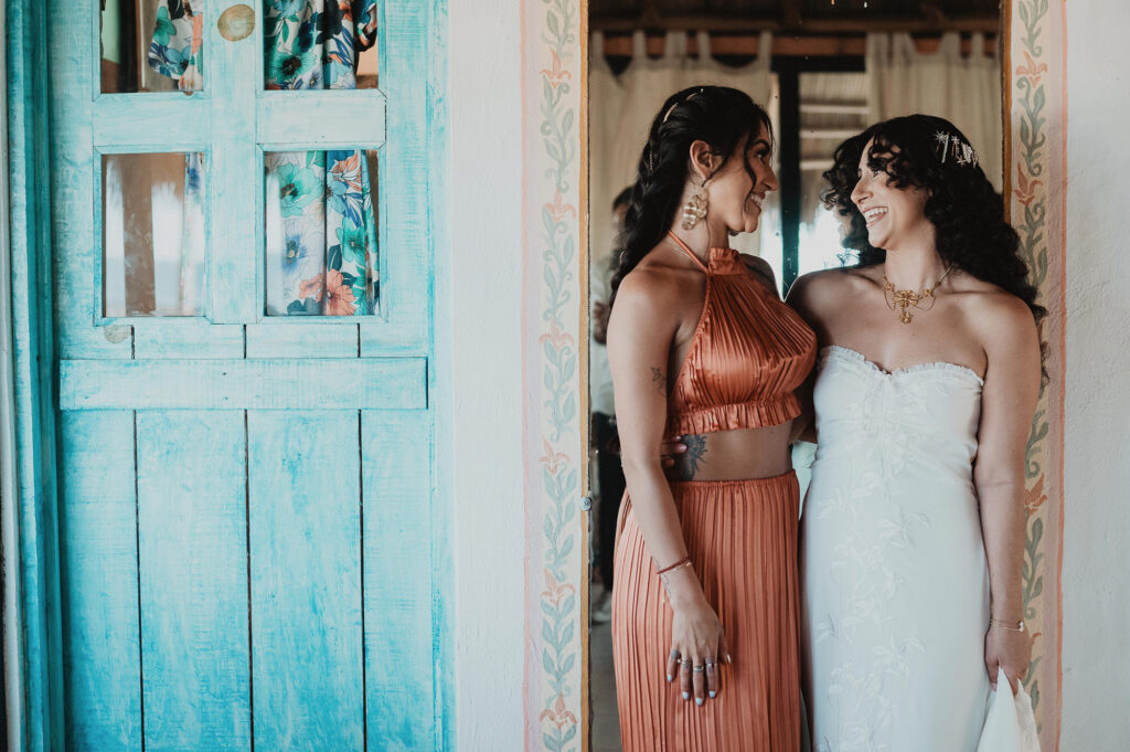 Bride and bridesmaid laughing together in colorful doorway at Frente al Punto, Sayulita wedding