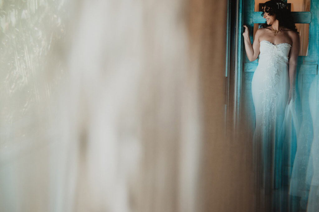 Bride in white lace gown standing in turquoise doorway at Frente al Punto, Sayulita wedding