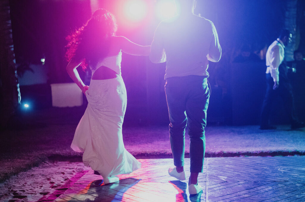 Bride and groom walking on dance floor at night reception, Frente al Punto Sayulita, colorful stage lights