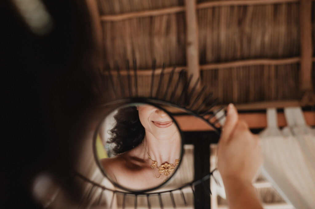 Bride smiling in handheld mirror reflection, gold necklace, thatched roof, Sayulita wedding, Alex Obregón