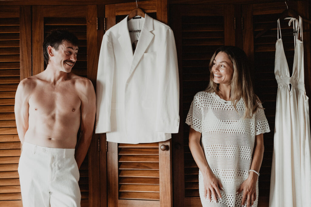 Bride and groom getting ready together at Villa del Sol Sayulita, laughing beside their white wedding outfits