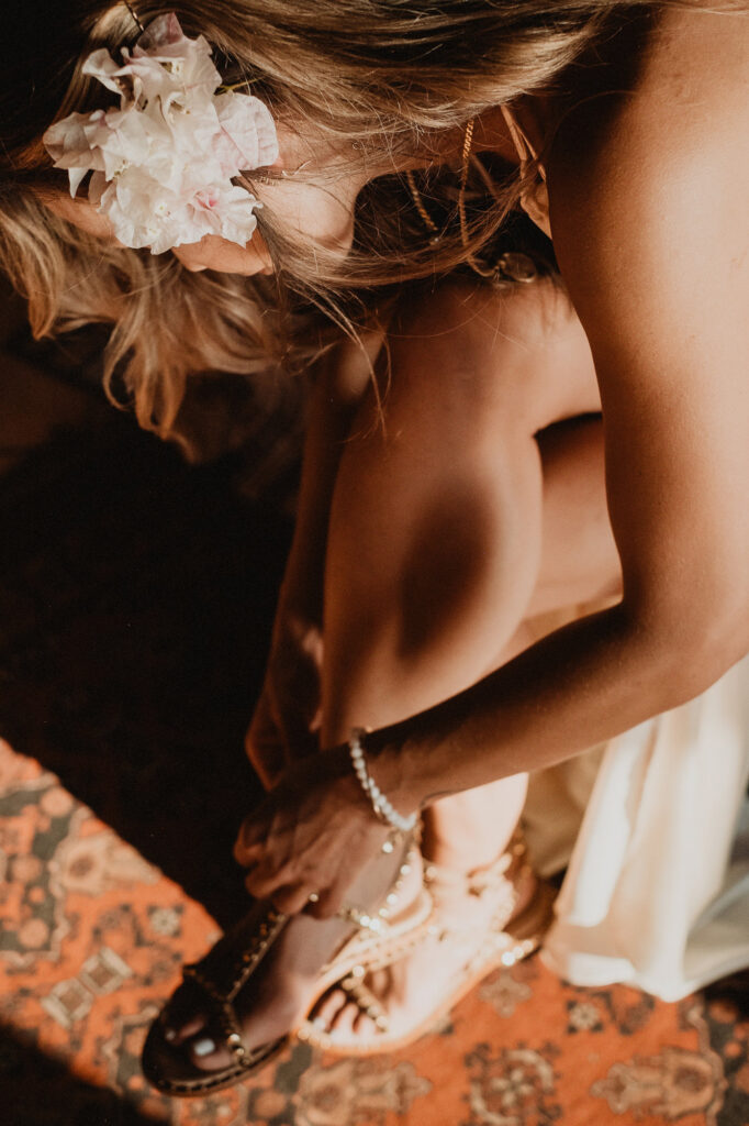 Bride adjusting pearl sandal at Villa del Sol Sayulita, flowers in hair, warm golden light
