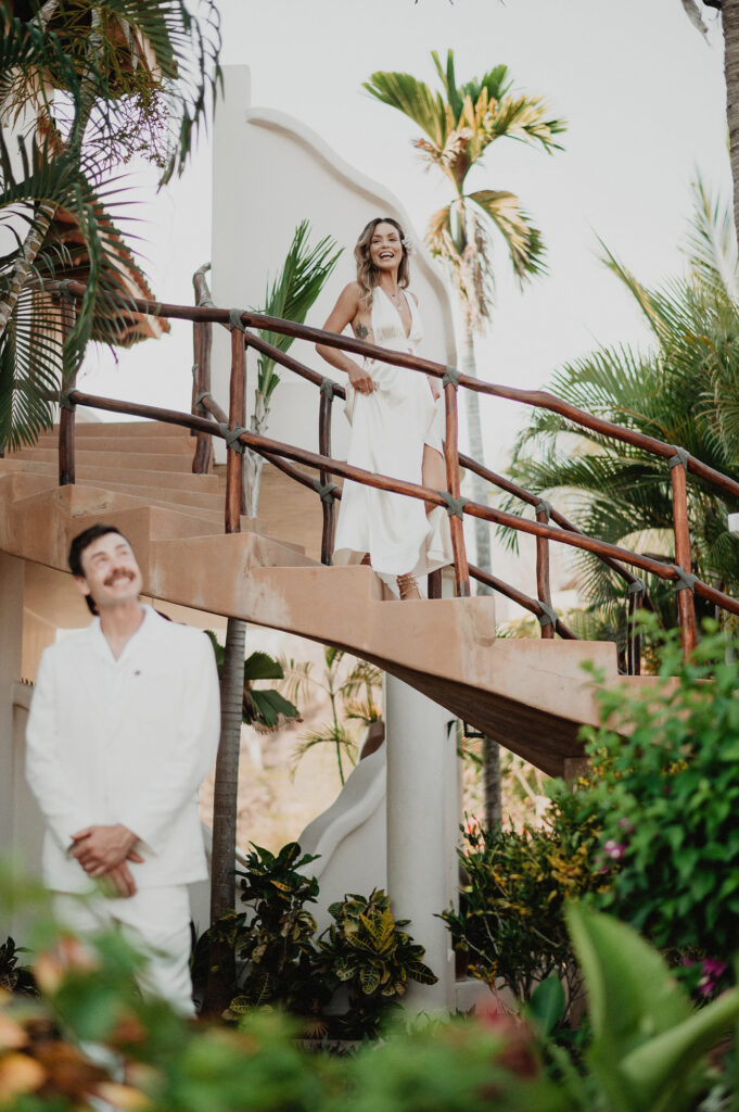 Bride laughing on staircase at Villa del Sol Sayulita wedding, groom waiting below in tropical garden