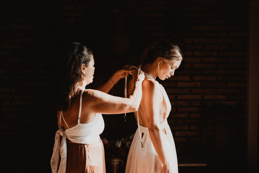 Bride getting dressed at Villa del Sol Sayulita, helper tying backless gown in warm golden light