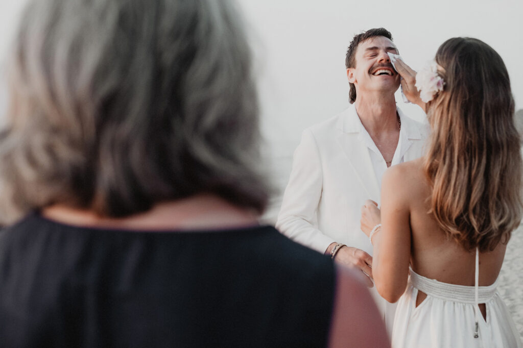 Groom laughing through tears as bride wipes his face during wedding ceremony at Villa del Sol Sayulita