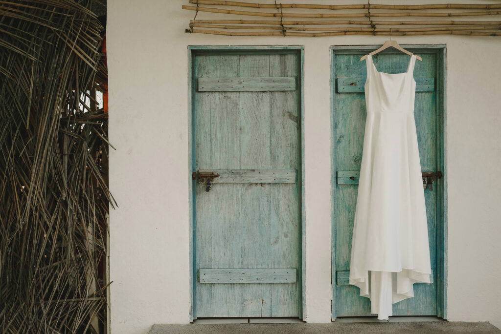 White wedding dress hanging on turquoise door at Frente al Punto, Sayulita wedding photography