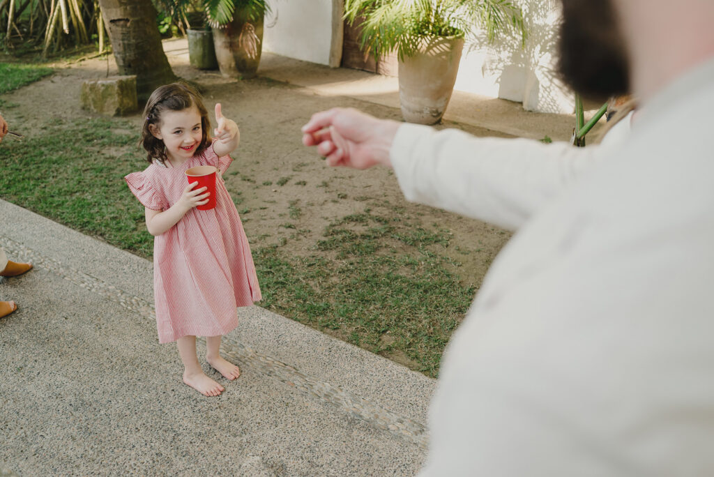 Young girl in pink dress holding red cup laughing at wedding reception, Frente al Punto Sayulita