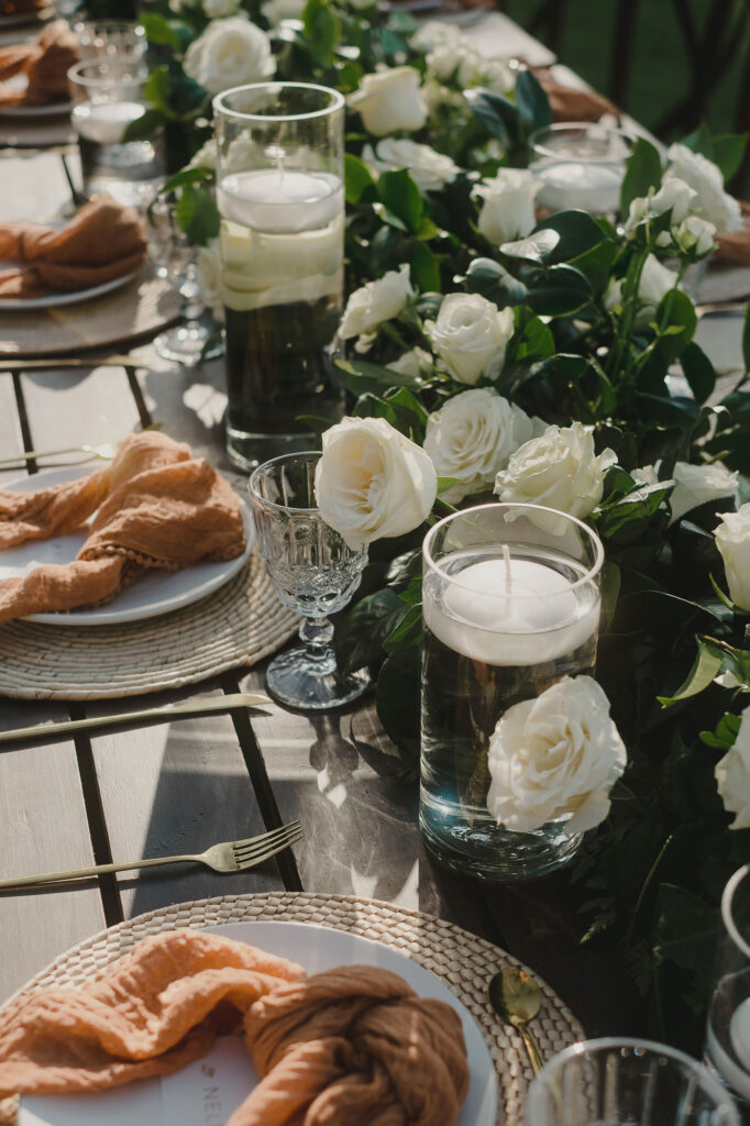 Wedding reception table with white roses, greenery runner, floating candles, terracotta napkins, Sayulita Mexico