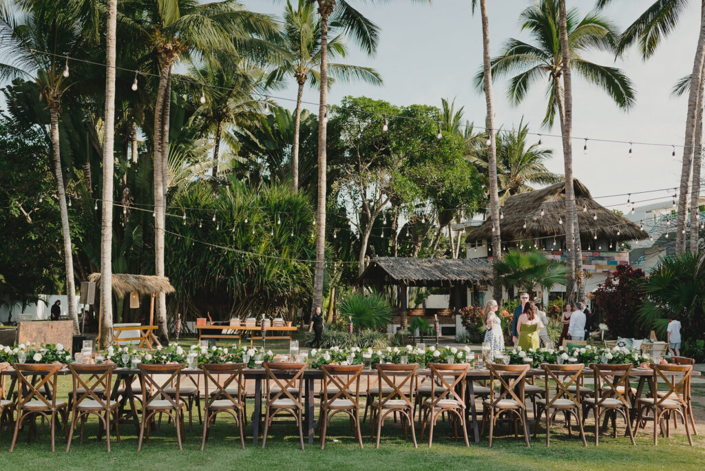 Outdoor wedding reception setup at Frente al Punto Sayulita with long wooden tables, white florals, and palm trees