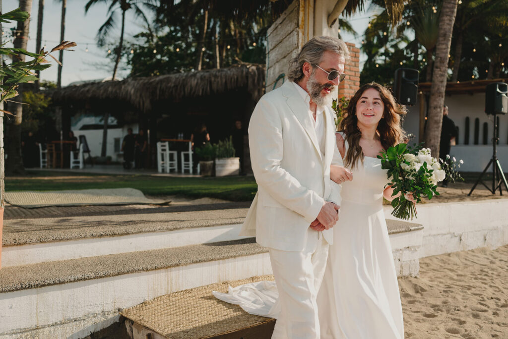 Bride and father walk together at Frente al Punto Sayulita beach wedding ceremony, white dress and bouquet