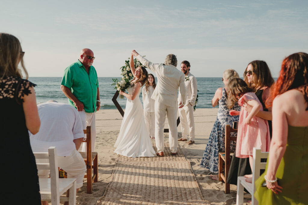 Beach wedding ceremony at Frente al Punto Sayulita, bride laughing as officiant raises her hand