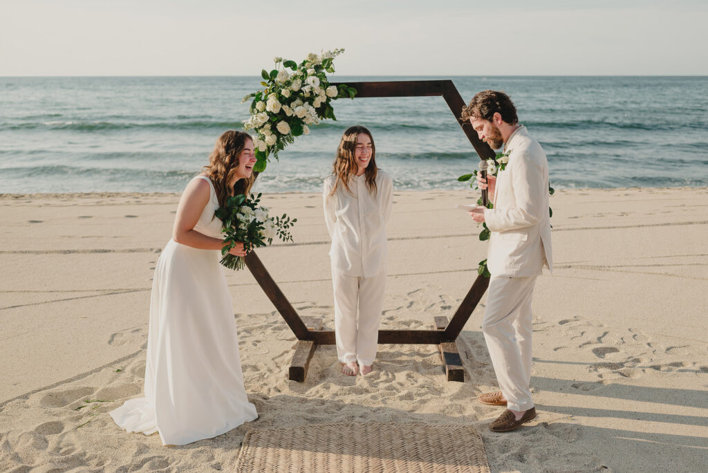 Beach wedding ceremony in Sayulita with bride and groom laughing under hexagonal floral arch