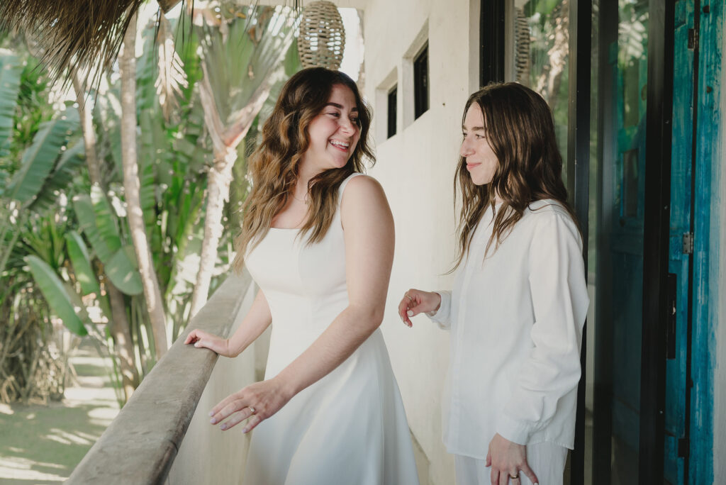 Two brides laughing together on a tropical balcony during their Sayulita wedding, photographed by Alex Obregón