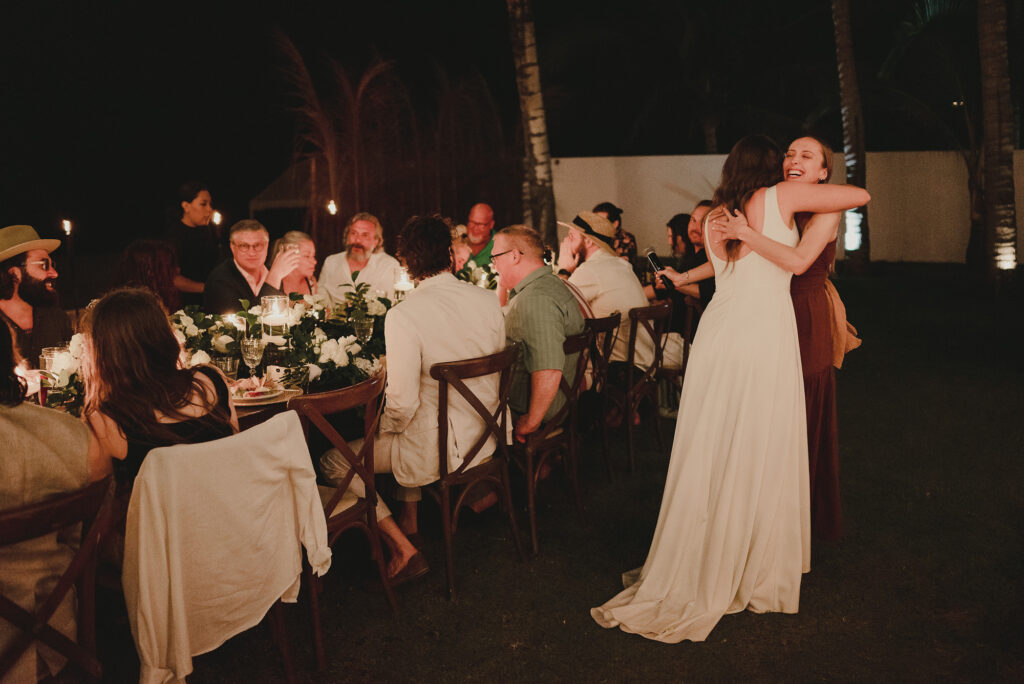 Bride hugging bridesmaid after toast at candlelit outdoor reception, Sayulita wedding photography