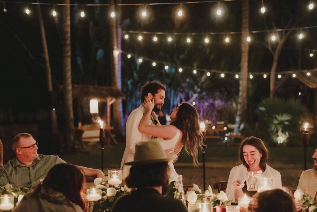 Couple sharing romantic moment at candlelit wedding reception at Frente al Punto, Sayulita, guests laughing around table