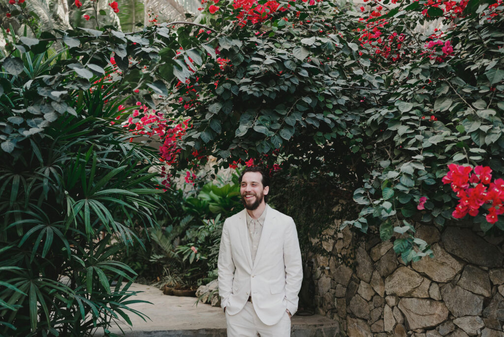 Groom laughing in white suit surrounded by bougainvillea at Frente al Punto wedding, Sayulita Mexico