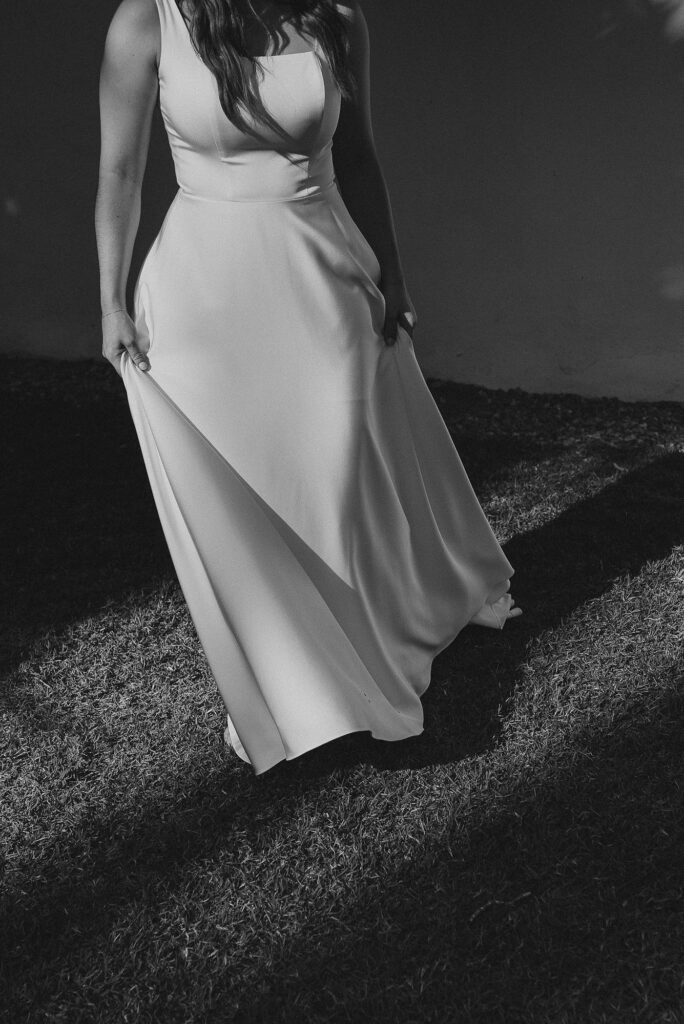Bride in flowing white gown standing on grass at Frente al Punto Sayulita wedding ceremony, black and white film style