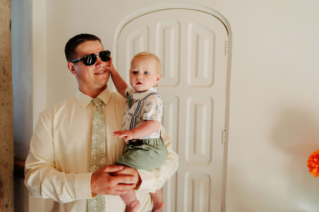 Groom in yellow shirt and floral tie holding baby at Villa Amor Sayulita wedding ceremony