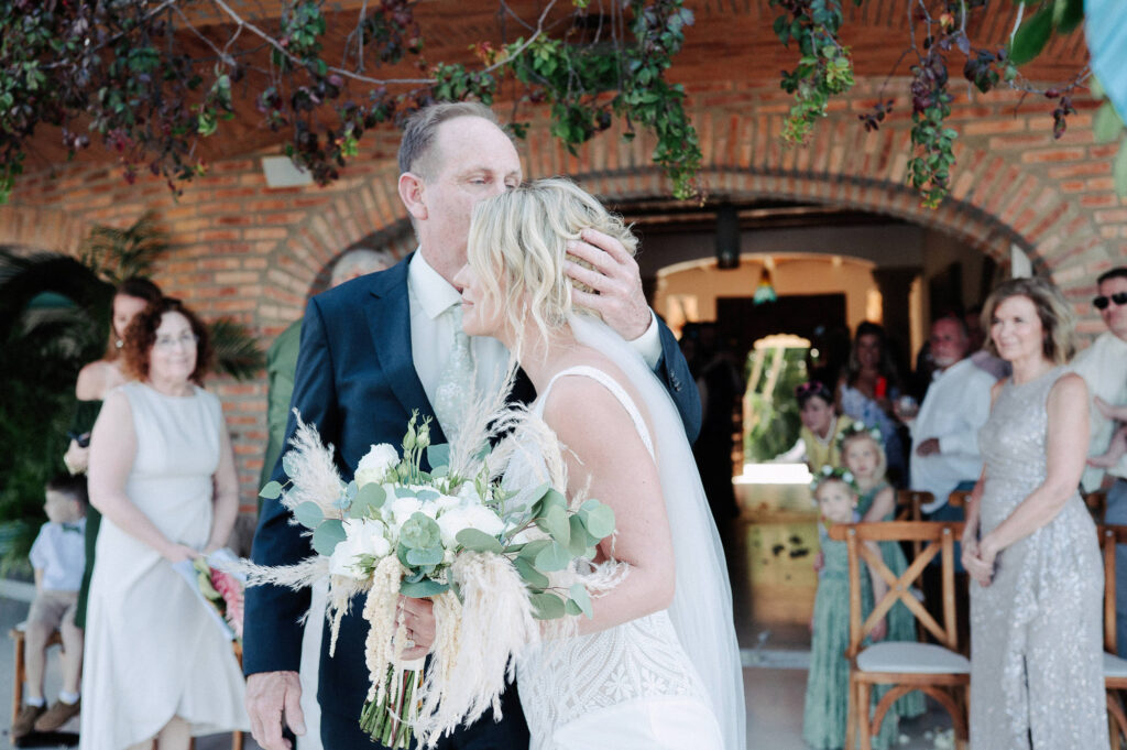 Father kisses bride during wedding ceremony at Villa Amor Sayulita, boho bouquet of pampas grass and white roses